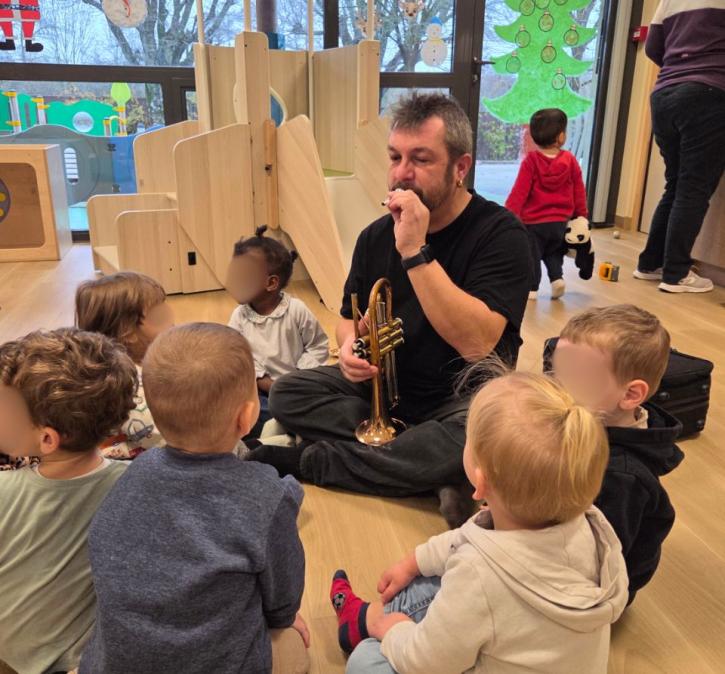 Vincent, de la cité éducative et artistique du Tonnerrois, joue de la trompette pour un groupe d'enfants assis sur le sol dans une salle de jeux.