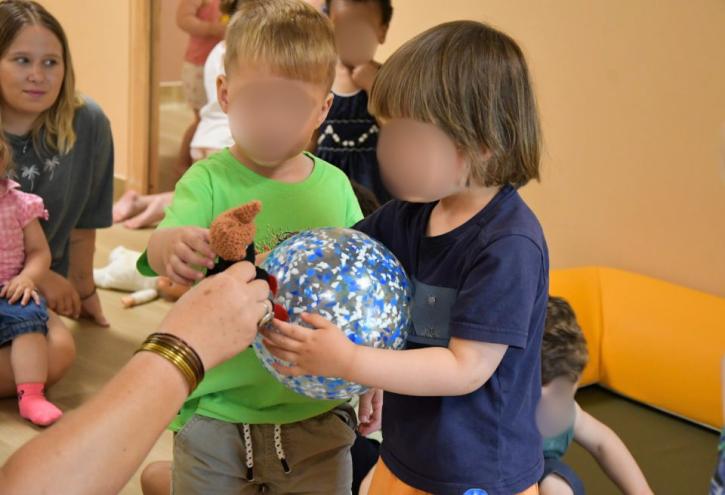 Deux jeunes enfants tenant un ballon et une petite poupée marron lors d'une activité ludique.